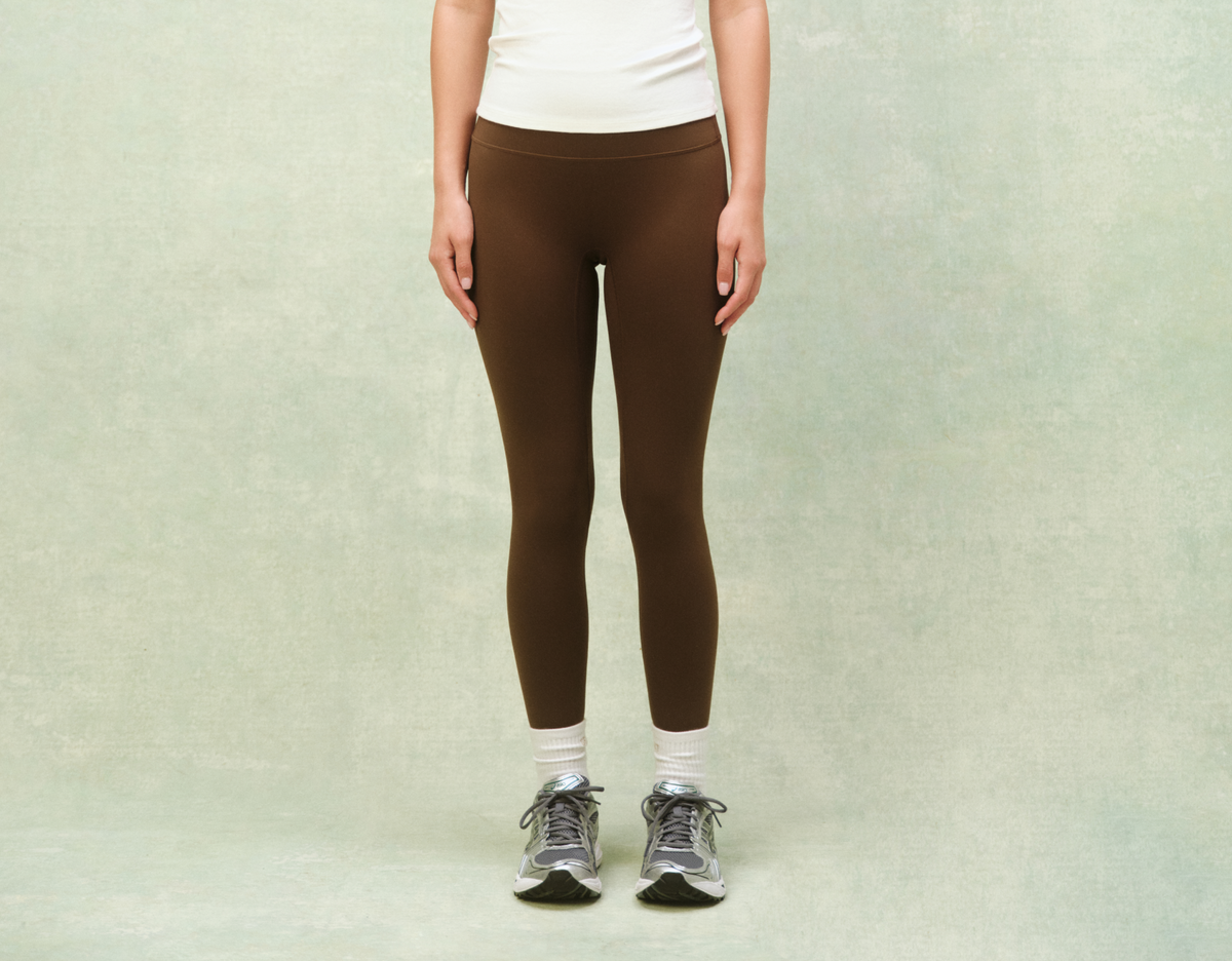 Person wearing brown leggings and white sneakers on a light green background