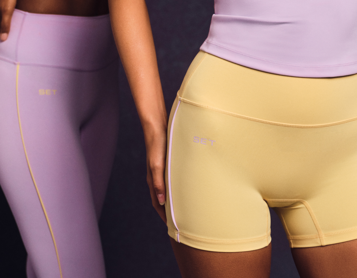 Two pairs of leggings, one purple and one yellow, worn by models against a dark background.