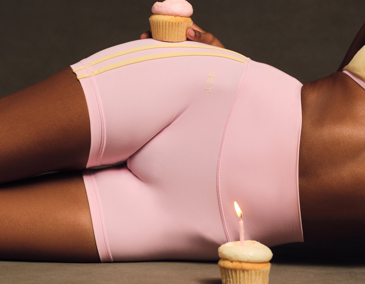 Person wearing pink underwear with a cupcake and candle on a dark background