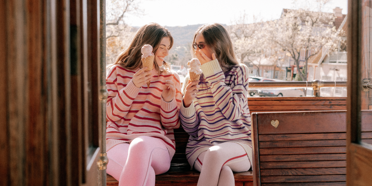 Two women sitting on a wooden bench outdoors, enjoying ice cream.
