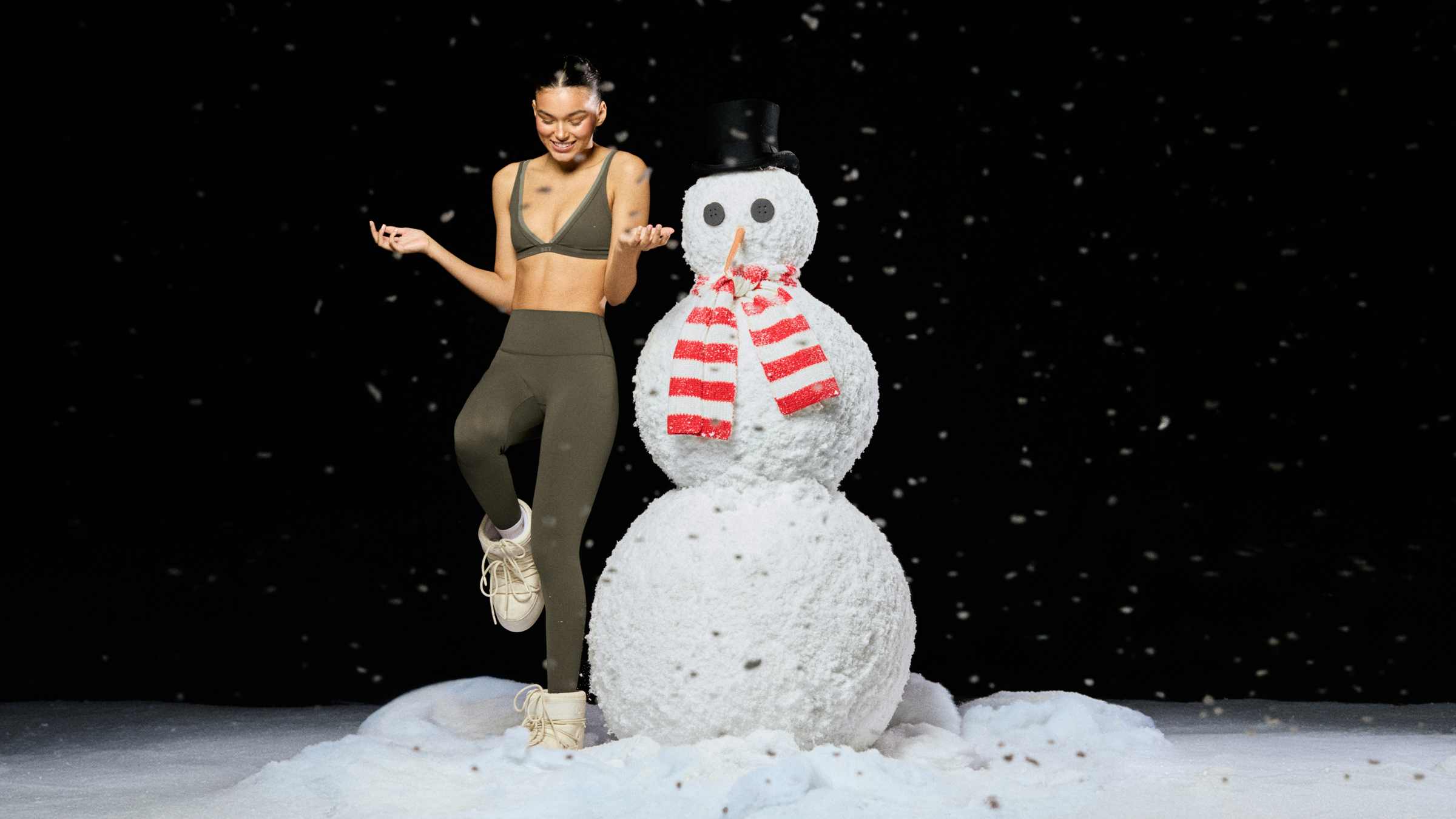 Woman in athletic wear standing next to a snowman with a red scarf on a snowy background