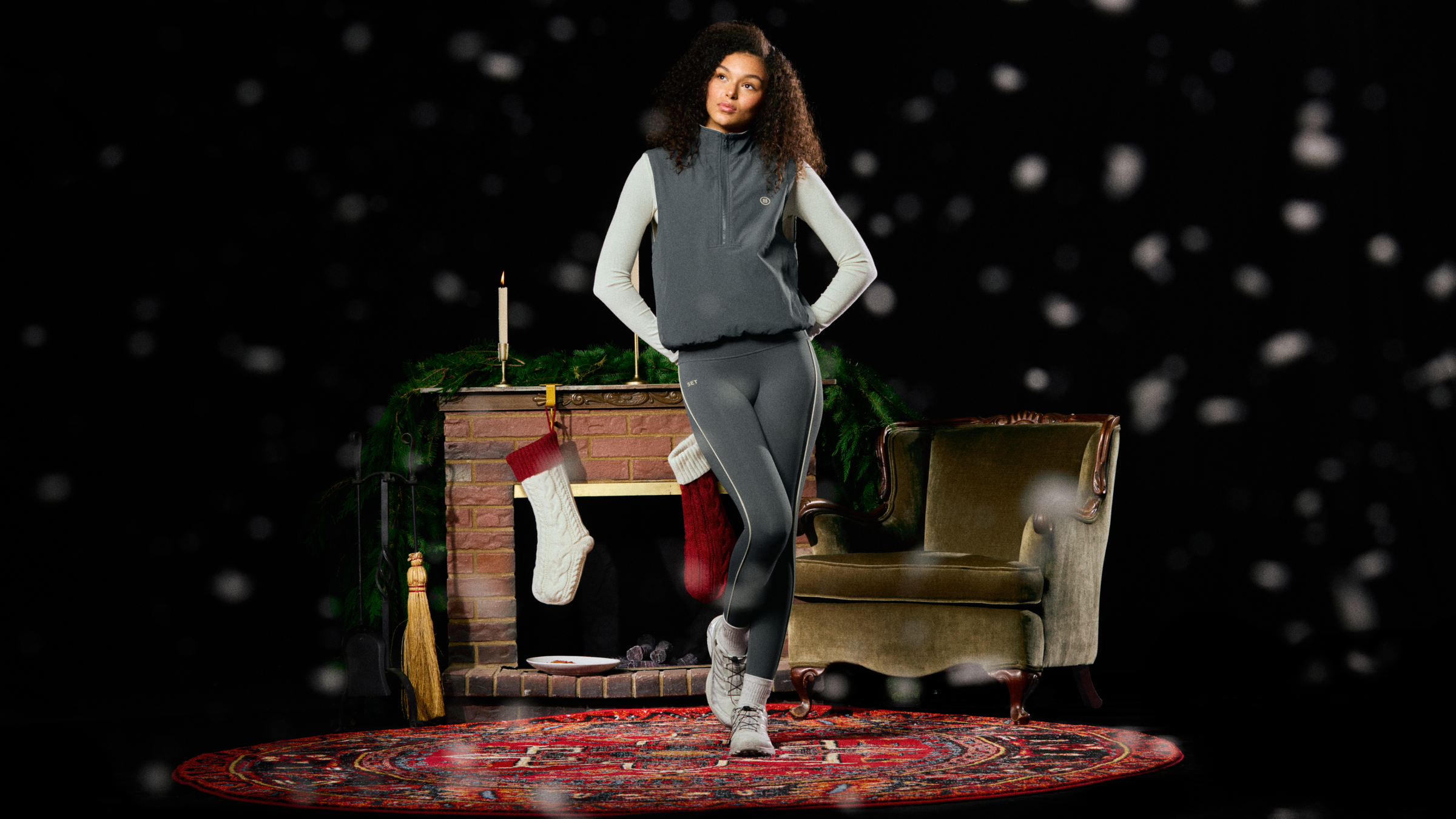 Woman in gray athletic wear standing in a room with a fireplace and stockings.
