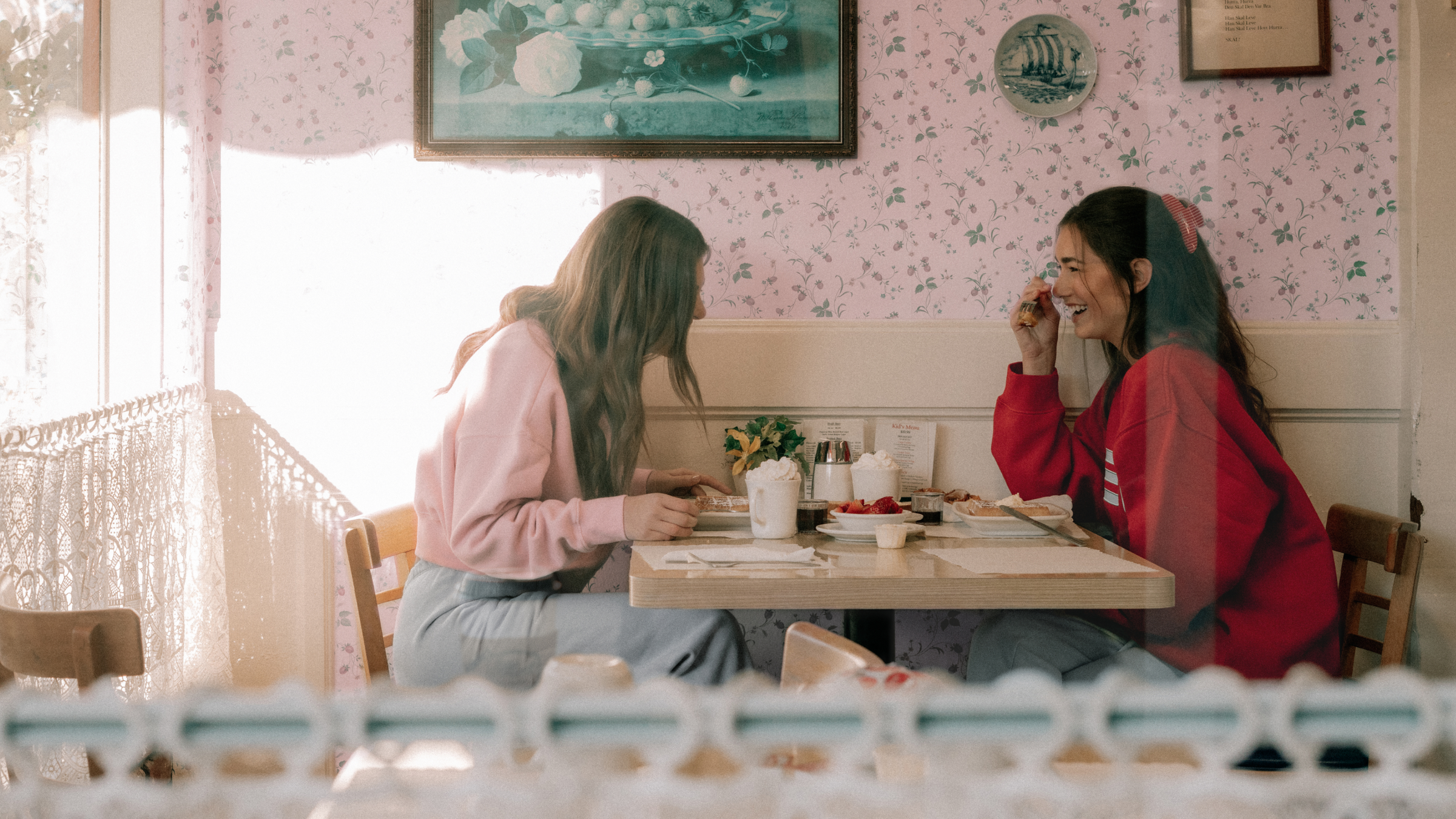Two women sitting at a table in a cozy restaurant with floral wallpaper.