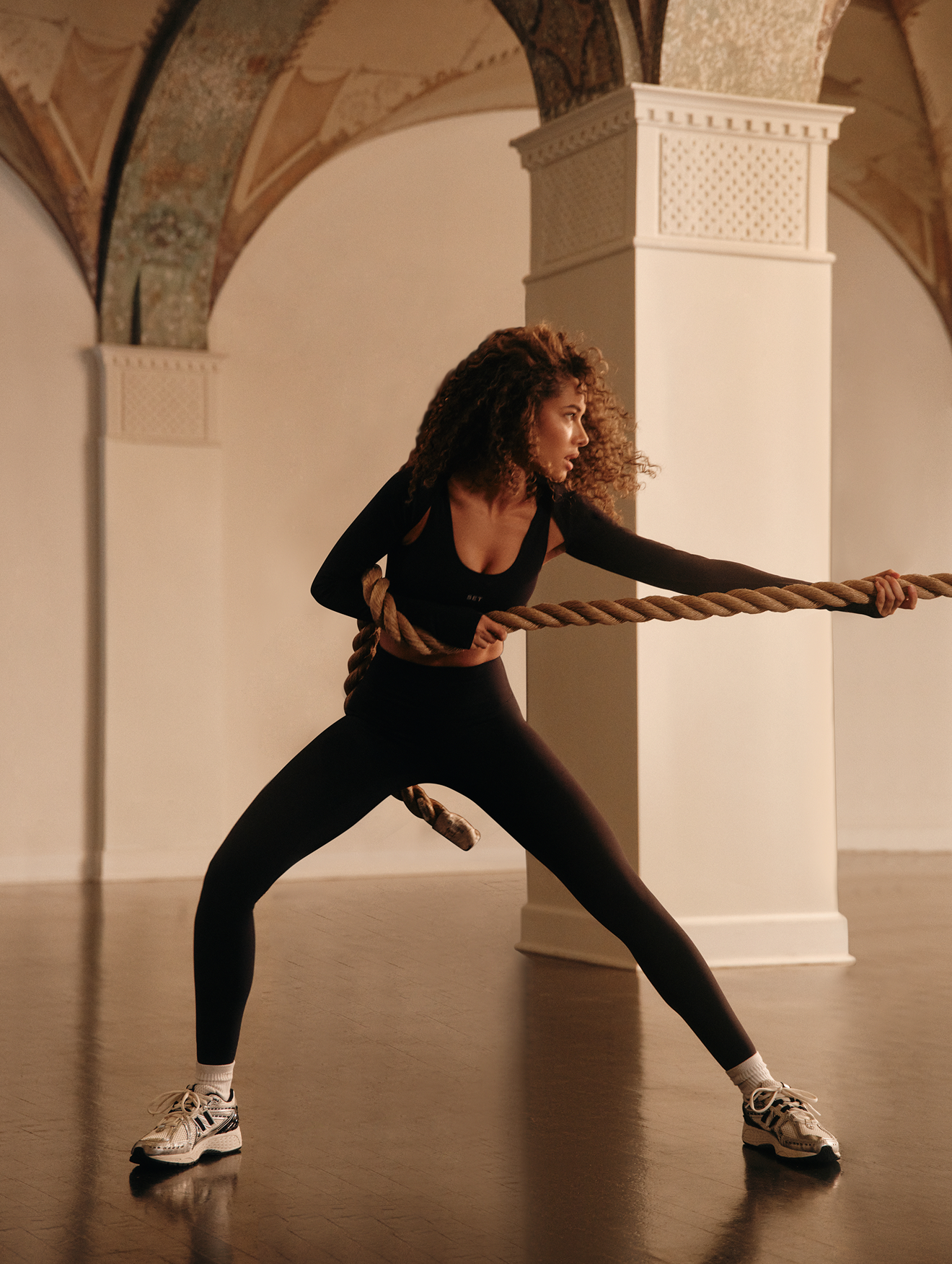 Woman pulling a rope in an indoor setting with architectural columns.