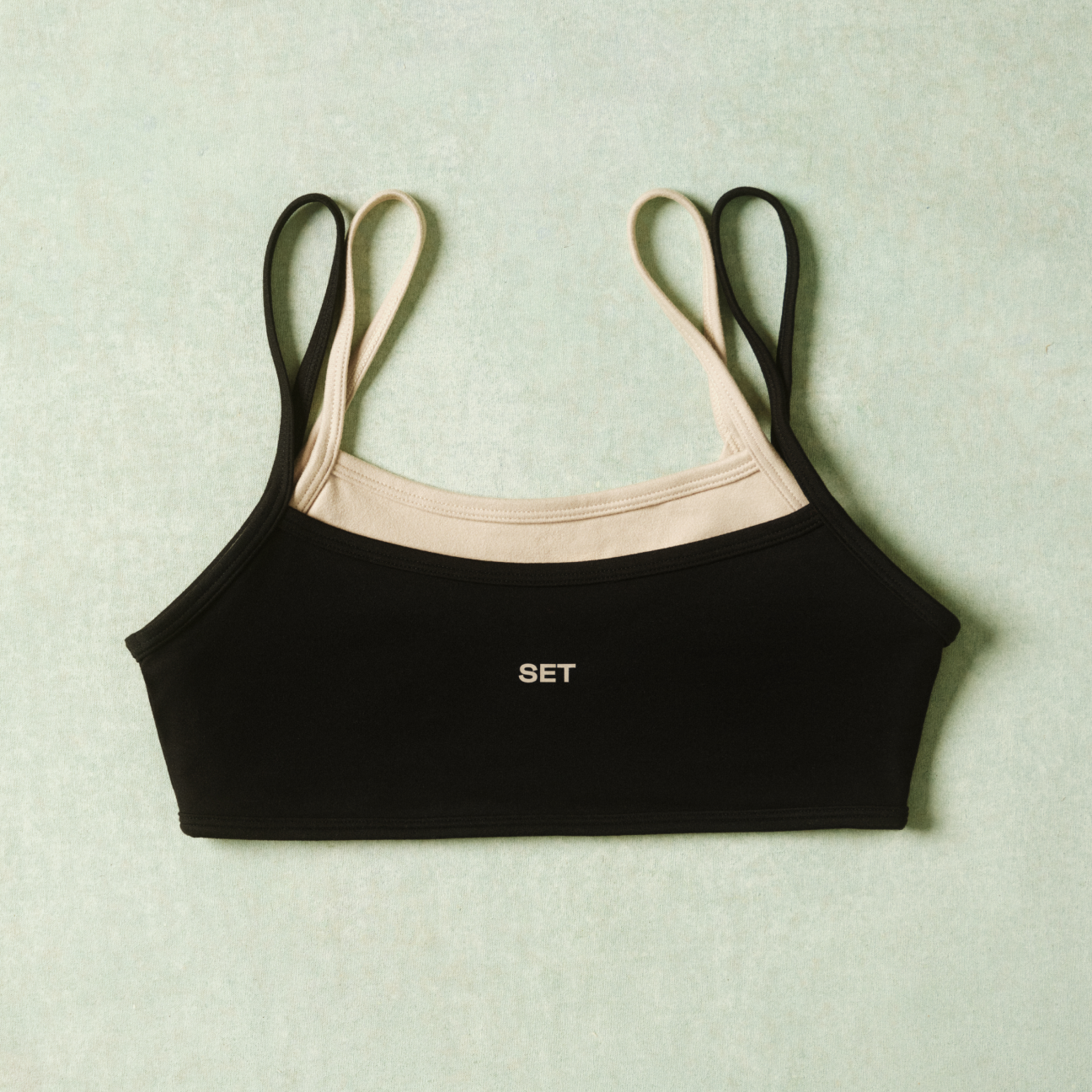 Black sports bra with beige lining on a light green background