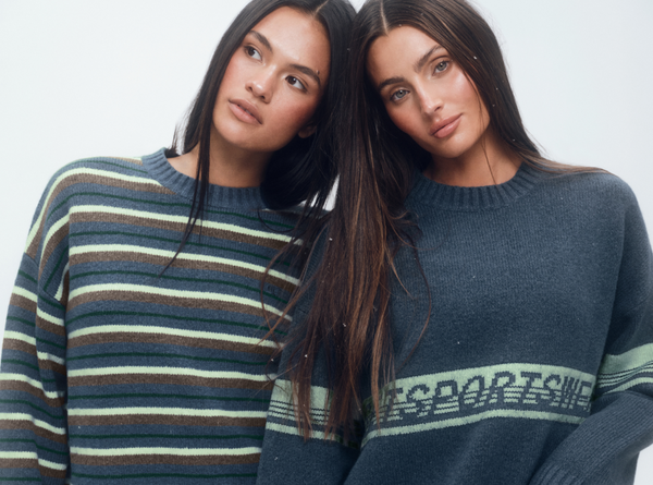 Two women wearing striped and patterned sweaters against a plain background
