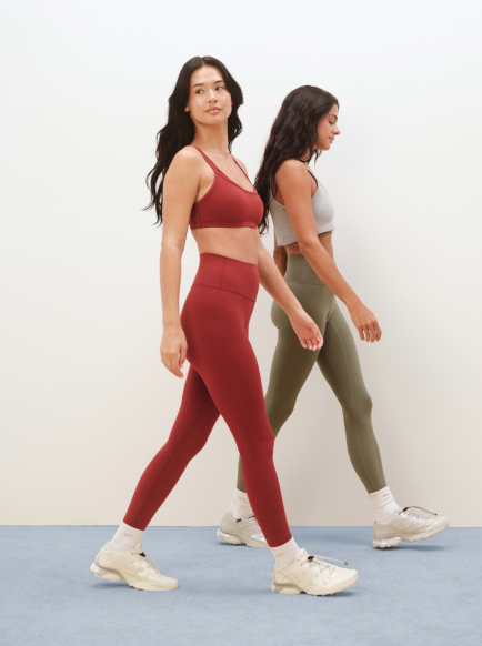Two women walking side by side, one in red athletic wear and the other in green athletic wear.