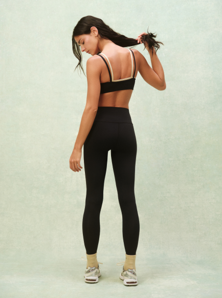Woman wearing a black sports bra and leggings on a light green background