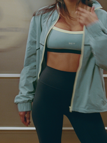 Person wearing a light blue athletic jacket and black leggings indoors.