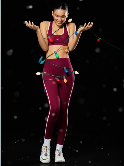 Woman in maroon athletic wear with Christmas lights against a dark background