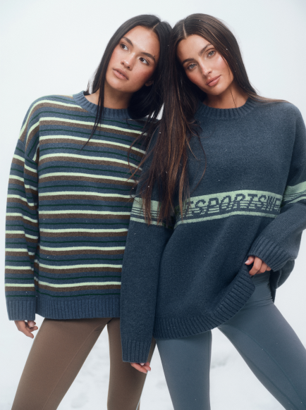 Two women wearing blue sweaters with a visible brand logo on a white background