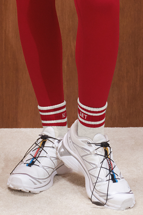 Person wearing red leggings with grey and red striped half crew socks and white athletic shoes.