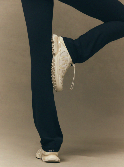Person wearing navy pants and white sneakers on a beige background