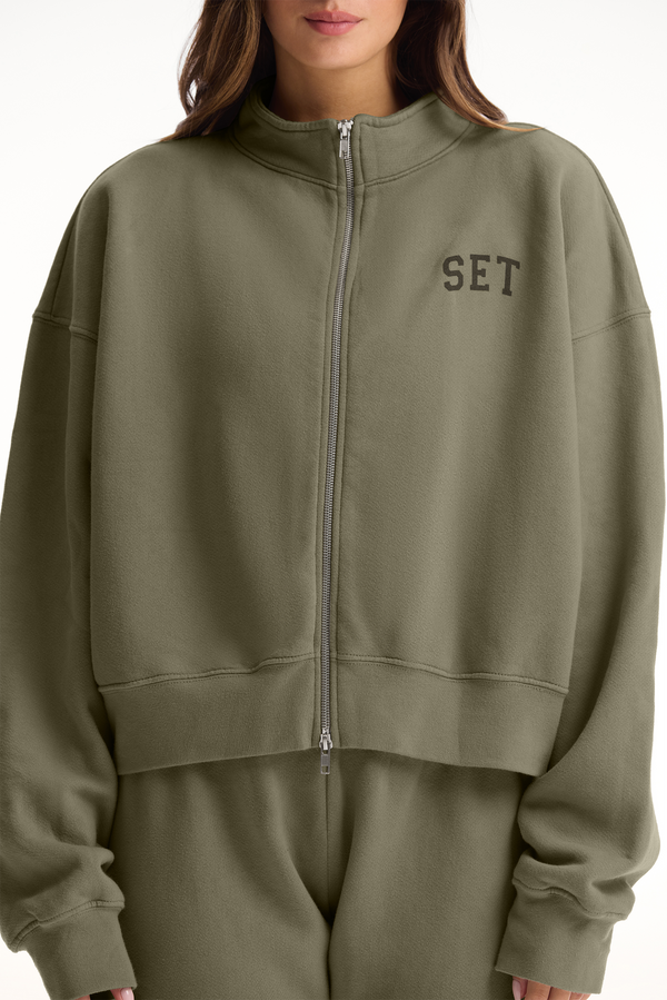Person wearing a green tracksuit with 'SET' logo on a white background