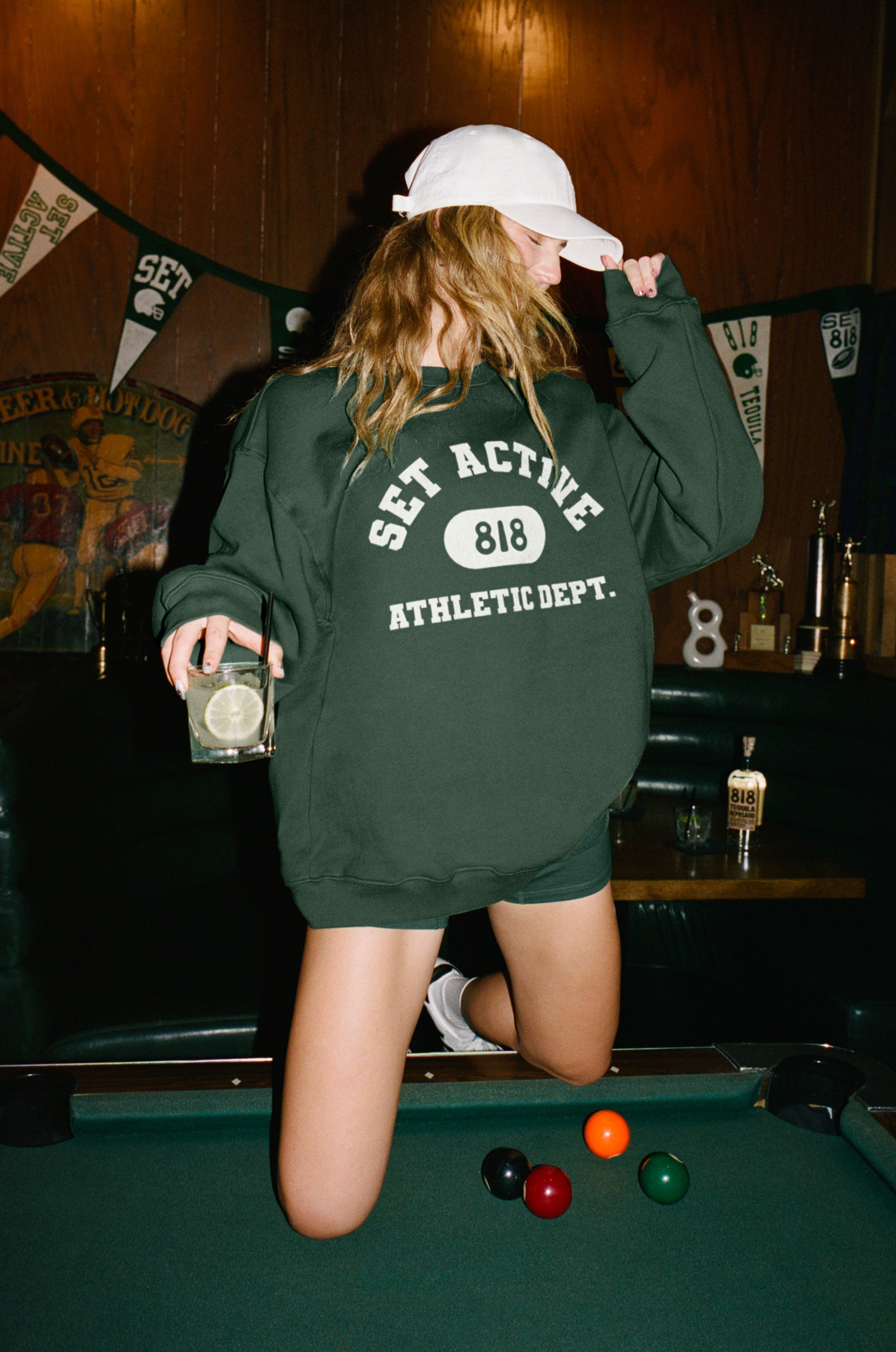 Girl wears green sweatshirt with 'SET Active' and '818' logos in a bar.