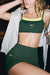 Woman wearing a green sports bra and shorts with 'SET' branding, standing indoors.