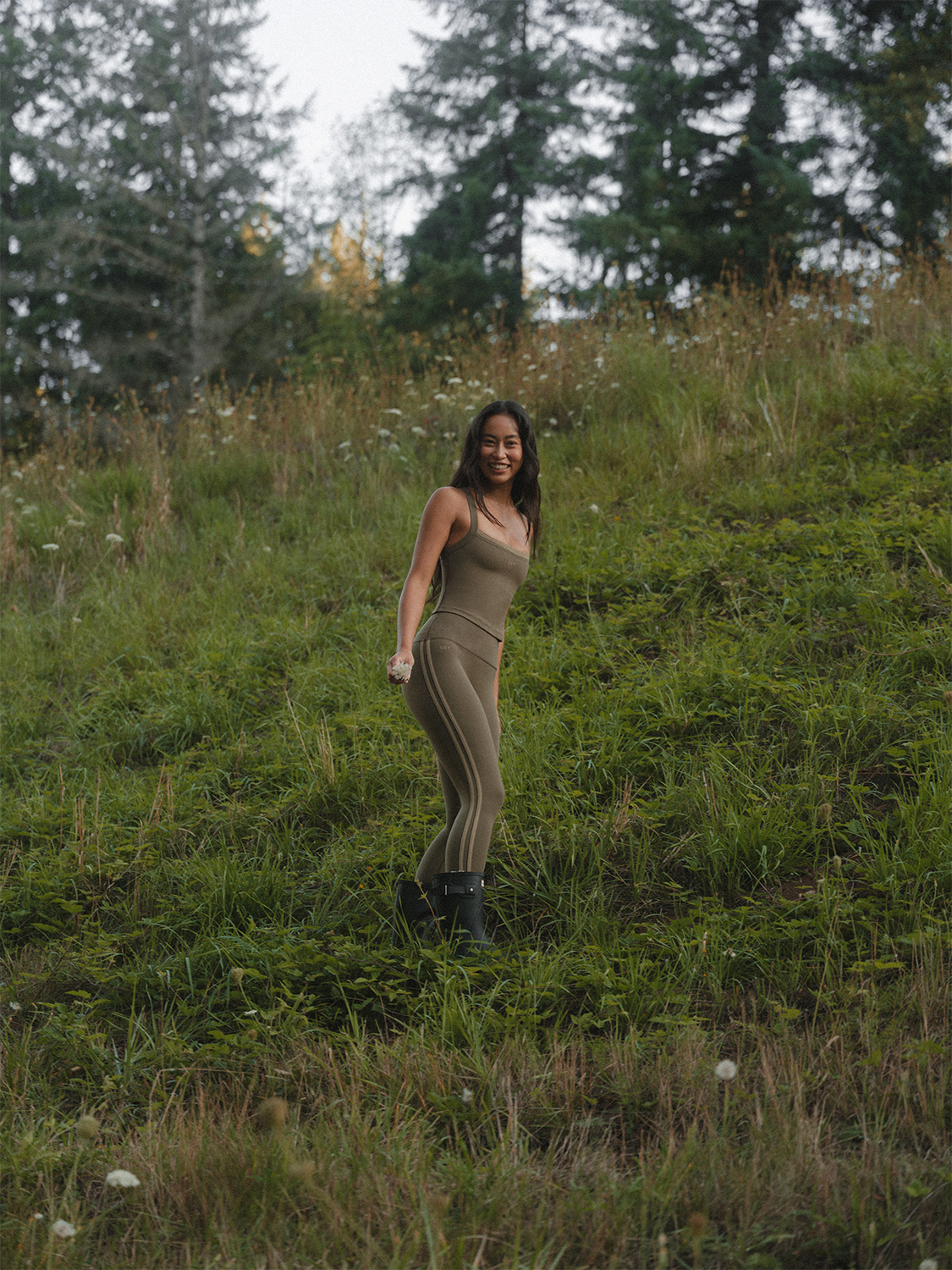 Woman in a green active set standing on a grassy hill with trees in the background