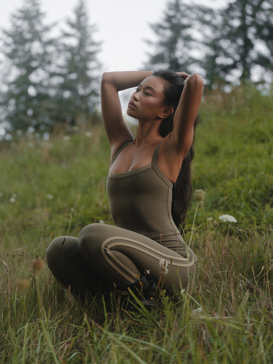 Woman in a green dress sitting in a field with trees in the background